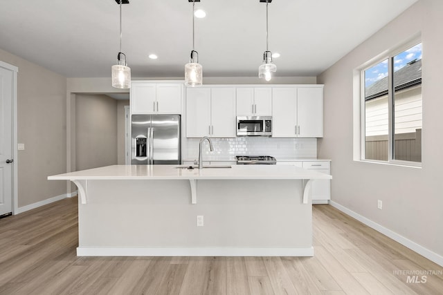 kitchen with stainless steel appliances, a kitchen island with sink, a sink, and hanging light fixtures