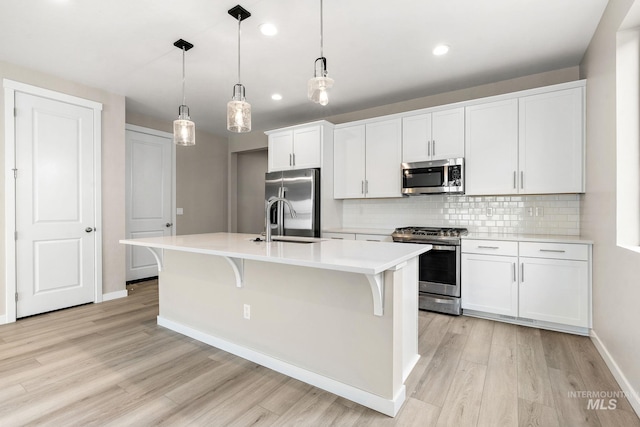 kitchen with white cabinets, a kitchen island with sink, stainless steel appliances, and decorative light fixtures