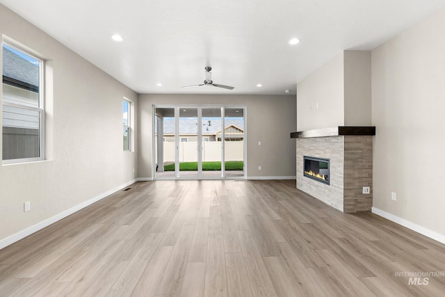 unfurnished living room with a stone fireplace, recessed lighting, light wood-style flooring, and baseboards