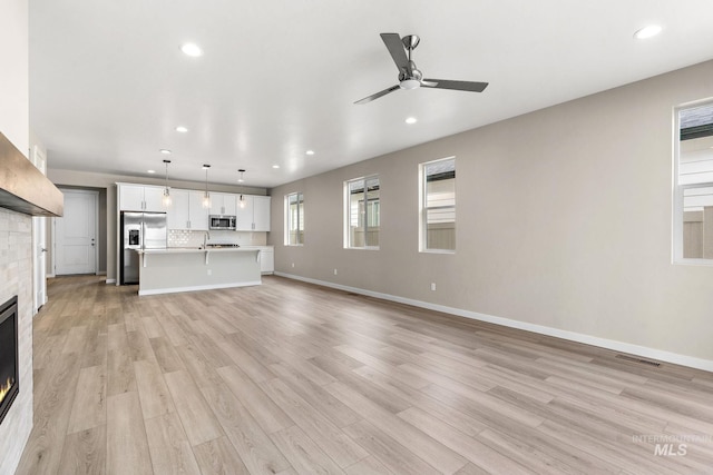 unfurnished living room with recessed lighting, visible vents, light wood-style flooring, a glass covered fireplace, and baseboards