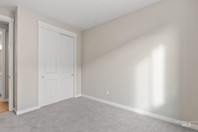 unfurnished bedroom featuring a closet, light colored carpet, and baseboards