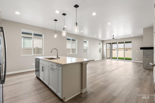 kitchen featuring an island with sink, open floor plan, light countertops, pendant lighting, and a sink