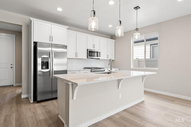 kitchen with appliances with stainless steel finishes, light countertops, a kitchen island with sink, and white cabinetry