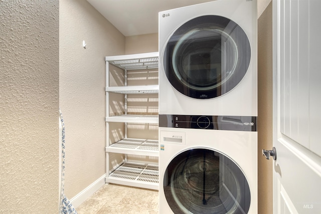 clothes washing area with baseboards, a textured wall, stacked washer / dryer, and laundry area
