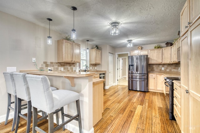kitchen featuring stainless steel appliances, light countertops, light brown cabinets, baseboards, and a peninsula