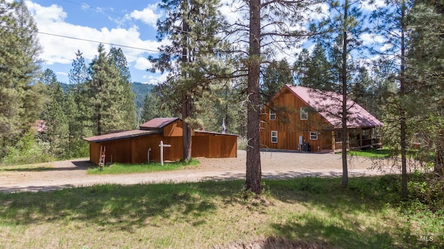 view of side of property with an outdoor structure, a view of trees, and an outbuilding