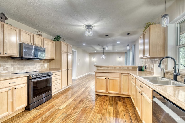 kitchen featuring a peninsula, appliances with stainless steel finishes, a sink, and light brown cabinetry