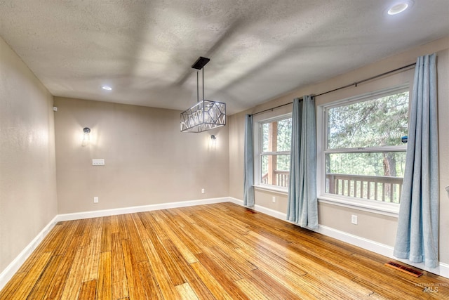 unfurnished dining area with baseboards, visible vents, wood finished floors, and a textured ceiling