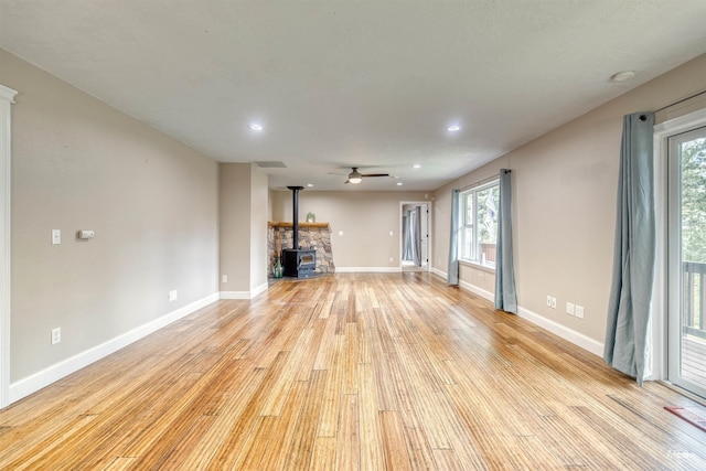 unfurnished living room featuring ceiling fan, a wood stove, light wood-style flooring, baseboards, and recessed lighting