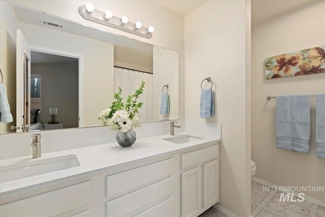 bathroom with toilet, baseboards, and double vanity