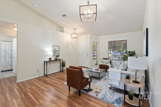 living area featuring lofted ceiling, a chandelier, wood finished floors, and baseboards