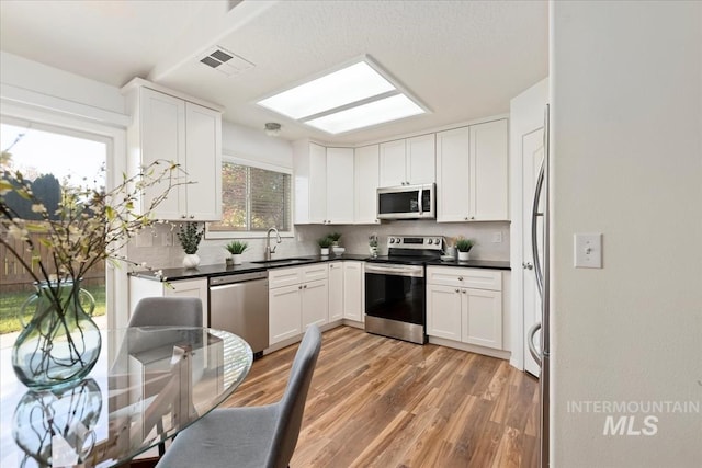 kitchen featuring stainless steel appliances, backsplash, a sink, light wood-style flooring, and dark countertops
