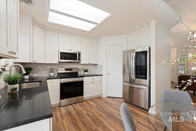 kitchen with appliances with stainless steel finishes, a sink, dark countertops, and white cabinets