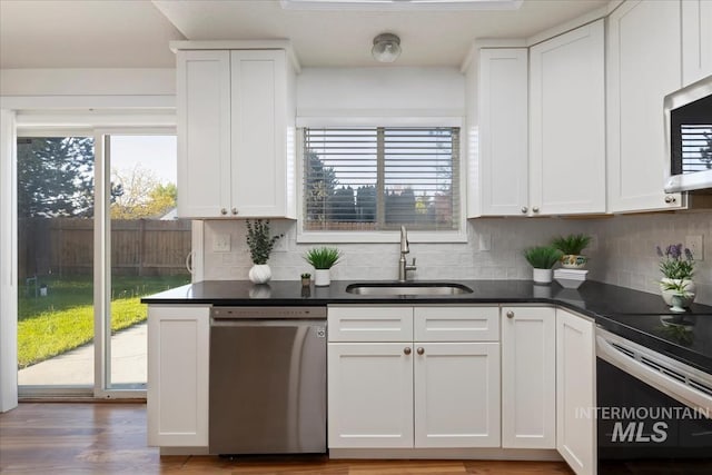 kitchen featuring stainless steel appliances, a sink, dark countertops, and white cabinetry