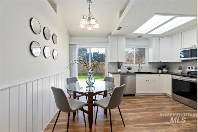 kitchen with stainless steel appliances, a sink, tasteful backsplash, a chandelier, and dark countertops