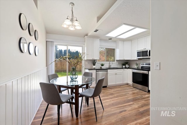kitchen featuring appliances with stainless steel finishes, a sink, a chandelier, tasteful backsplash, and dark countertops
