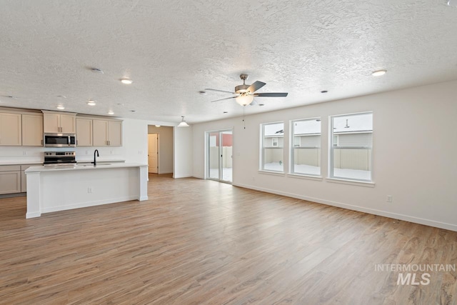 kitchen with open floor plan, light wood-style floors, appliances with stainless steel finishes, light countertops, and ceiling fan