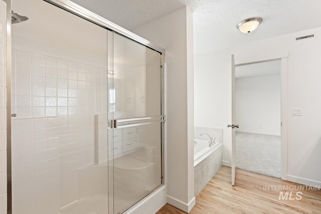 bathroom featuring a garden tub, wood finished floors, a stall shower, and a textured ceiling