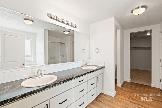 full bath featuring a sink, wood finished floors, a textured ceiling, and a stall shower