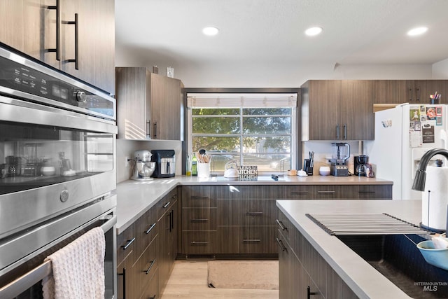 kitchen with white fridge, sink, light wood-type flooring, and stainless steel double oven