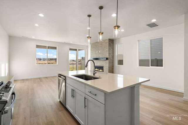 kitchen featuring light wood finished floors, visible vents, a stone fireplace, stainless steel appliances, and a sink