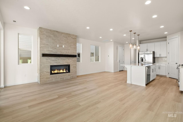 kitchen featuring a stone fireplace, a center island with sink, appliances with stainless steel finishes, and light wood-style floors