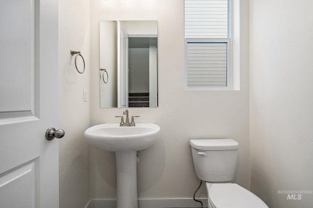 half bathroom featuring toilet, baseboards, and a sink