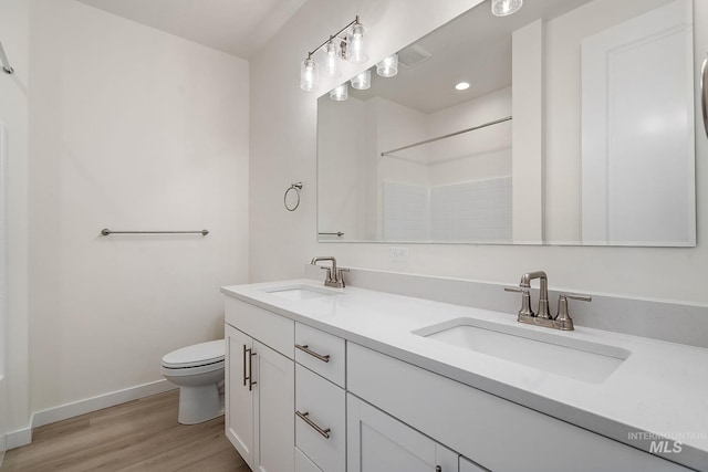 full bathroom featuring toilet, wood finished floors, baseboards, and a sink