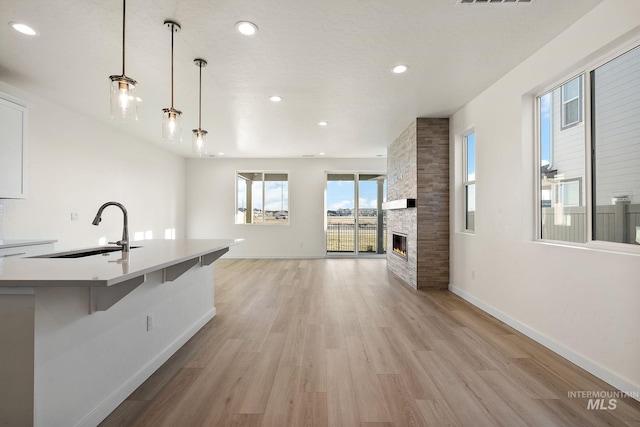 kitchen with a sink, baseboards, light wood-style flooring, and a fireplace