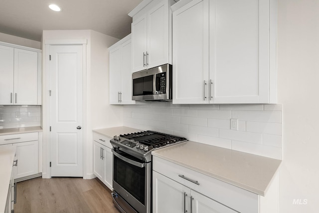 kitchen with light countertops, white cabinets, light wood-style floors, appliances with stainless steel finishes, and tasteful backsplash