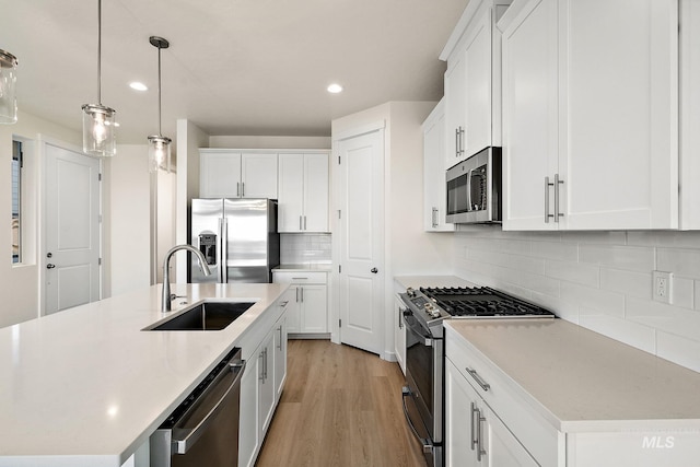 kitchen featuring a kitchen island with sink, a sink, stainless steel appliances, light wood-style floors, and light countertops