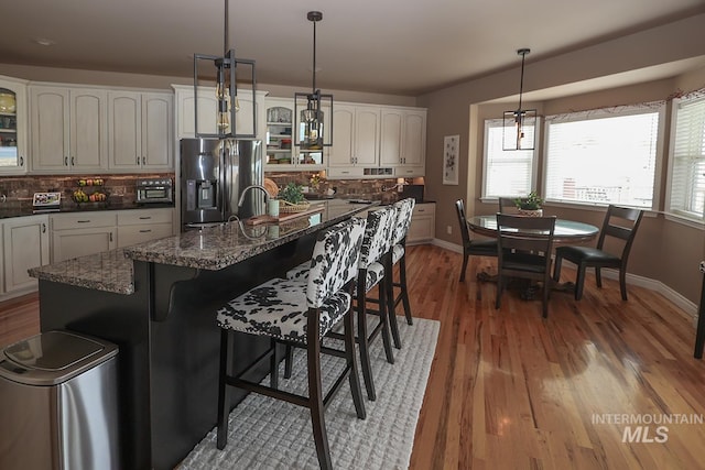 kitchen with stainless steel refrigerator with ice dispenser, wood-type flooring, a center island, and hanging light fixtures