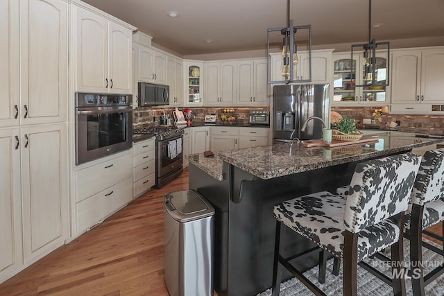 kitchen with appliances with stainless steel finishes, light hardwood / wood-style floors, a kitchen island with sink, hanging light fixtures, and a breakfast bar