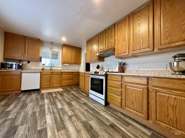 kitchen with dark wood-type flooring, stainless steel appliances, light stone countertops, and sink