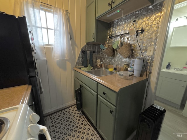 kitchen featuring radiator heating unit, sink, green cabinets, range, and black fridge