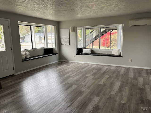 empty room featuring a wall mounted air conditioner, a textured ceiling, baseboards, and wood finished floors