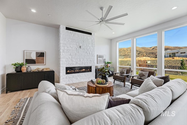 living room featuring a fireplace, ceiling fan, a mountain view, and light wood-type flooring