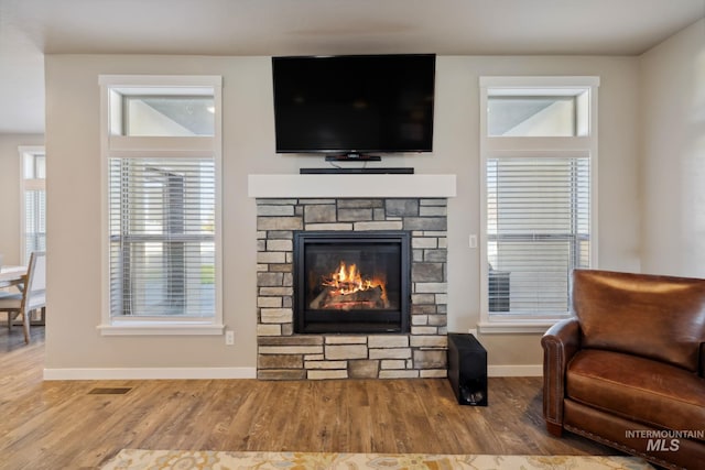 living area with visible vents, a stone fireplace, baseboards, and wood finished floors
