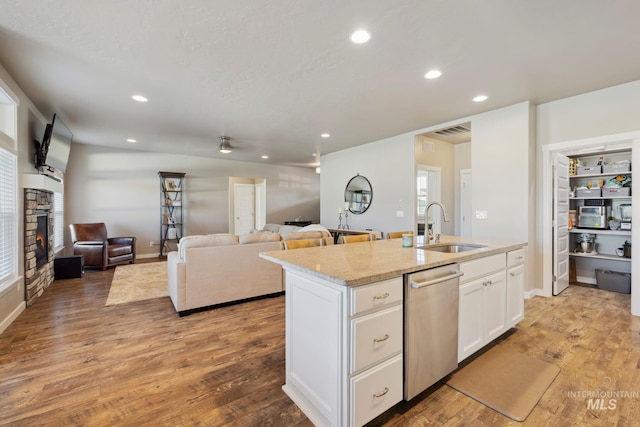 kitchen featuring open floor plan, stainless steel dishwasher, a sink, light wood-style floors, and a stone fireplace