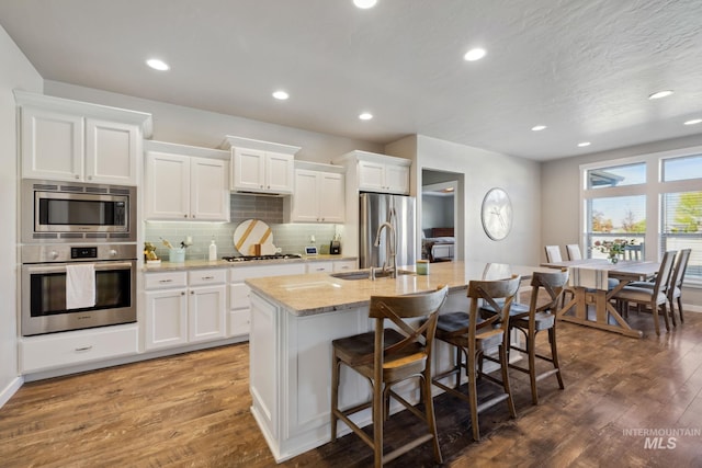 kitchen with a sink, a breakfast bar area, wood finished floors, stainless steel appliances, and a kitchen island with sink