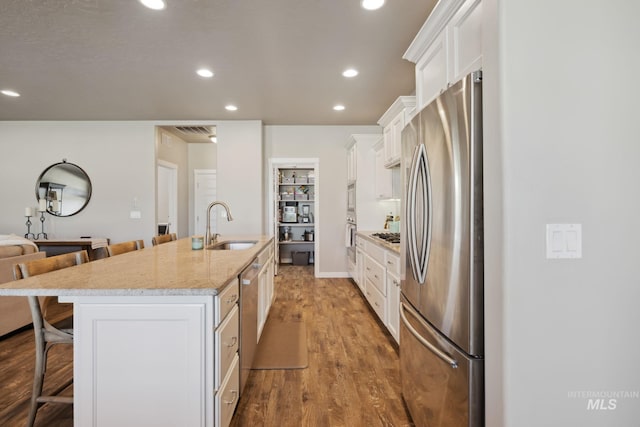 kitchen featuring a kitchen breakfast bar, white cabinetry, a center island with sink, a sink, and appliances with stainless steel finishes