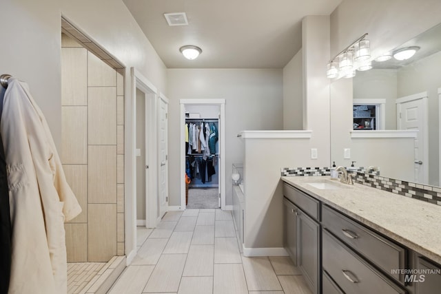 full bath featuring vanity, tasteful backsplash, a spacious closet, baseboards, and visible vents