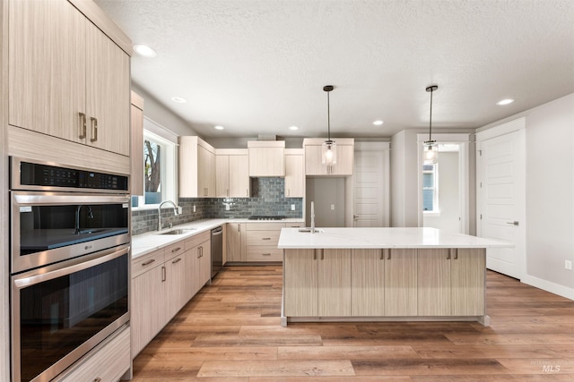 4469 E Wingate Ct, Nampa, ID 83687 - kitchen featuring light brown cabinetry, appliances with stainless steel finishes, a sink, an island with sink, and backsplash