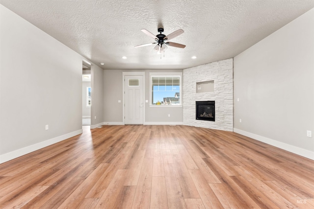 4469 E Wingate Ct, Nampa, ID 83687 - unfurnished living room with ceiling fan, light wood-style flooring, a textured ceiling, a stone fireplace, and healthy amount of natural light