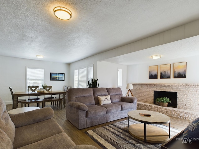 living room with a brick fireplace, wood-type flooring, and a textured ceiling