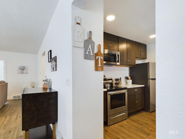 kitchen featuring appliances with stainless steel finishes, dark brown cabinetry, lofted ceiling, and light wood-type flooring