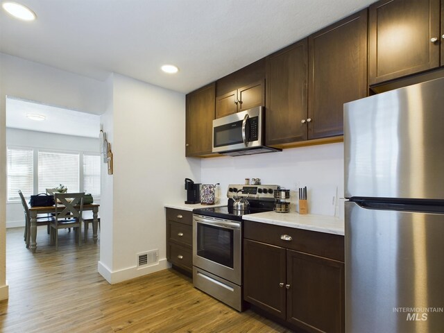 kitchen with light wood-type flooring, dark brown cabinetry, and stainless steel appliances