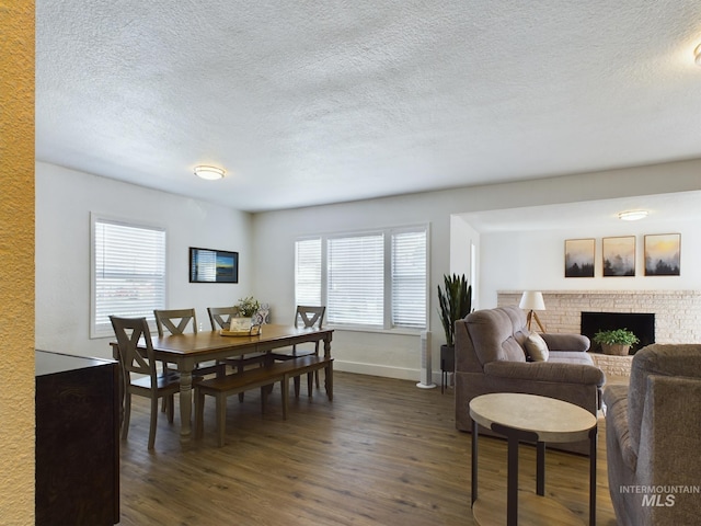 dining area with a brick fireplace, a textured ceiling, dark wood-type flooring, and a healthy amount of sunlight