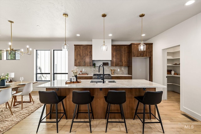 1796 S Eagleson Rd, Boise, ID 83705 - kitchen featuring light wood-type flooring, tasteful backsplash, a sink, a kitchen island with sink, and dark brown cabinets