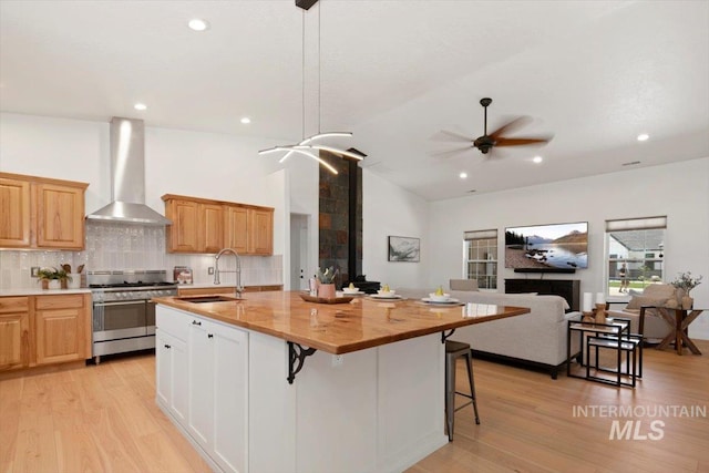 kitchen featuring range with two ovens, open floor plan, a kitchen island with sink, wall chimney range hood, and a sink